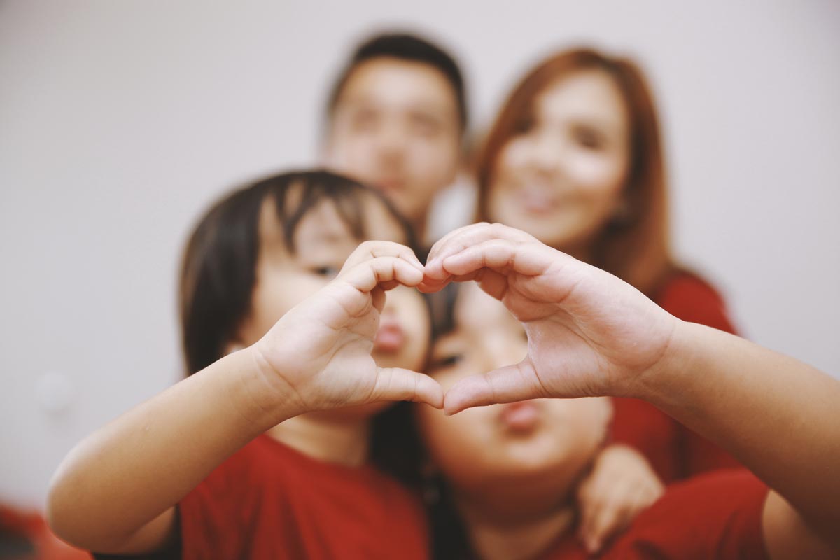 A family portrait with two little asian girls making a heart in the front of their parents 